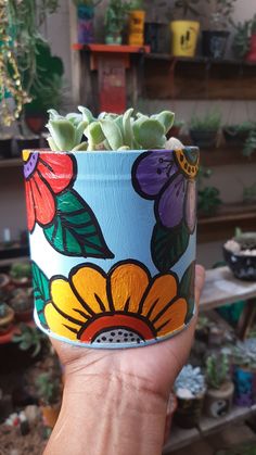 a hand holding up a painted flower pot with succulents in the background