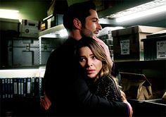 the man and woman are hugging each other in front of shelves with boxes on them