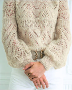 a woman wearing a sweater and white pants with her hands in her pockets, holding onto the