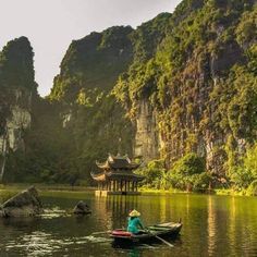 a person on a small boat in the water with mountains behind them and trees around it