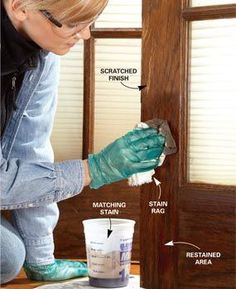 a woman in blue jeans and green gloves painting a door with white paint on it