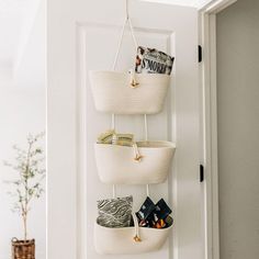 three white baskets hanging from the wall in front of a door with magazines on it