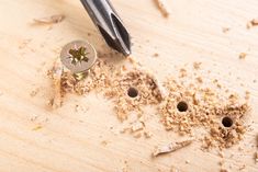 a wooden cutting board with some wood shavings on it and a drill in the middle