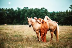 a woman is laying on the back of a horse in a field with trees behind her