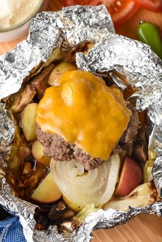 a hamburger covered in cheese and onions on top of aluminum foil next to some vegetables