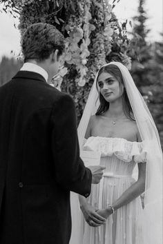 a man and woman standing next to each other in front of a flower covered structure