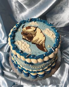 a blue and white cake with a dog on it's side sitting on a silver cloth