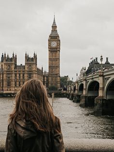 a woman standing in front of the big ben clock tower and river thames, london