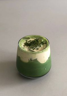 a green and white dessert in a glass on a gray surface with sprinkles