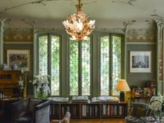 a living room filled with lots of furniture next to large windows and a chandelier hanging from the ceiling