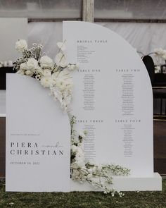 a wedding seating plan with white flowers and greenery on the back of an arch