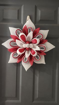 a red and white wreath hanging on the front door, with an ornament shaped like a flower