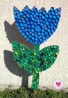 a blue and green flower made out of bottle caps on the side of a building