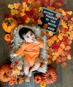 a baby in an orange bodysuit laying on top of pumpkins