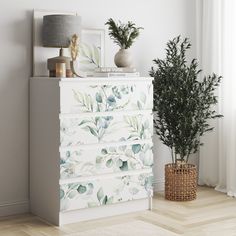 a white dresser sitting next to a potted plant on top of a wooden floor