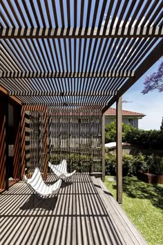 two white lawn chairs sitting on top of a wooden deck under a pergolated roof