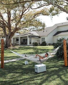 a man laying in a hammock on top of a grass covered field next to a house