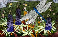 a stained glass window with dragonflies and flowers in the foreground, surrounded by foliage