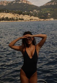 a woman in a black one piece swimsuit standing on the edge of a body of water