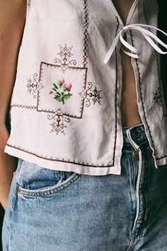 a close up of a person wearing jeans and a shirt with embroidered flowers on it