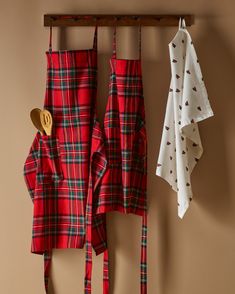 two red aprons hanging on a rack next to some white and green plaid towels