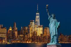 the statue of liberty is lit up at night in front of the new york city skyline