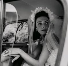 a woman in a wedding dress sitting in a car with her hand on the door handle