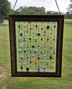 a stained glass window hanging from a chain on a grassy field with trees in the background