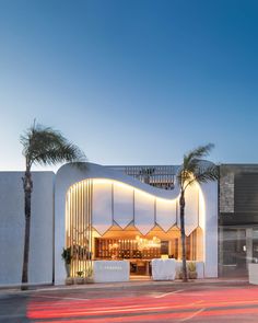 the exterior of a building with palm trees in front of it and lights on at night