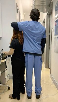 two people in scrubs standing next to each other looking at something on the wall