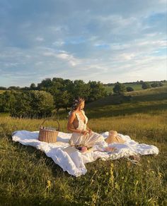 a woman sitting on top of a white blanket in a field next to a basket