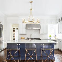 a large kitchen with white cabinets and blue island in the center is surrounded by gold bar stools