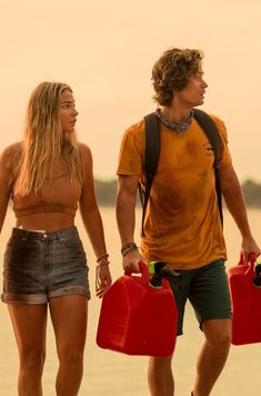 a man and woman walking on the beach with two red buckets in their hands