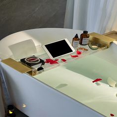 a bath tub with a tablet on top of it and some bottles next to it