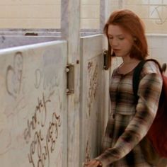 a woman with red hair is leaning against a wall and looking down at the door