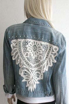 a woman wearing a jean jacket with white lace on the chest and back, standing in front of a wall