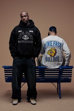 two men standing next to each other on a blue bench with one man wearing a black hoodie