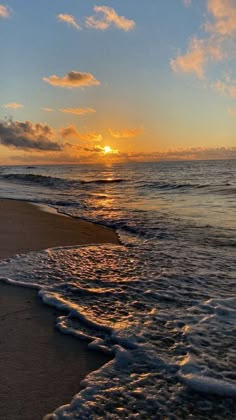 the sun is setting over the ocean with waves coming in to shore and clouds above