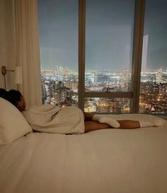 a woman laying on top of a bed in a bedroom next to a large window