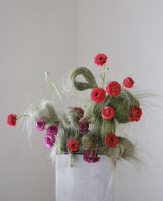 a white vase filled with lots of red and pink flowers on top of a table