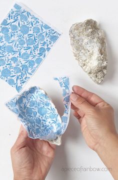 someone is peeling an egg shell with blue and white designs on it, next to a rock