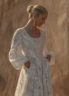 a woman standing in front of a wall wearing a white dress