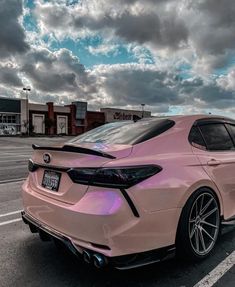 a pink car is parked on the side of the road with clouds in the background