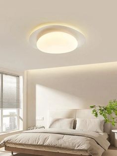 a white bed sitting under a round light in a bedroom next to a large window