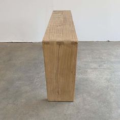 a wooden bench sitting on top of a cement floor next to a white wall in an empty room