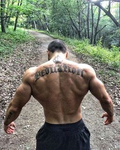 a man with tattoos on his back walking down a dirt road in the woods,