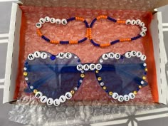 two pairs of sunglasses with beads and name tags on them sitting in a cardboard box