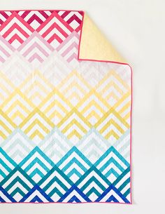 a multicolored blanket laying on top of a white table next to a yellow wall