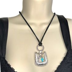 a woman's torso wearing a black top with a silver and turquoise pendant on it