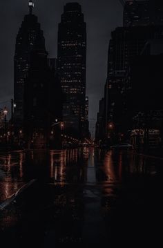 a city street at night with lights reflecting off the wet pavement and skyscrapers in the background